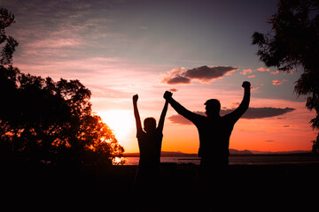 silhouette of father and son against nature background with raised hands,concept of family success