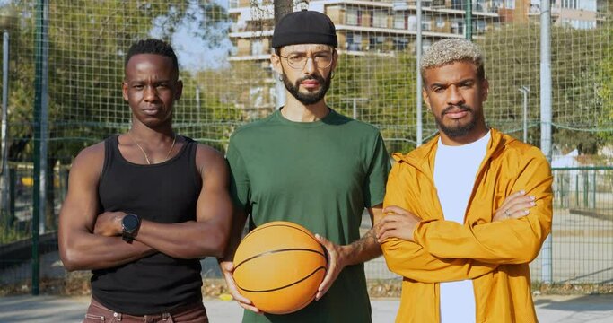 Portrait of three diverse young men looking seriously at camera on a basketball court with a ball in their hand