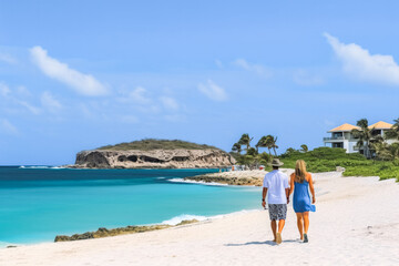 Fototapeta na wymiar A couple on a beach. Man and woman walking on the coast of Tres Trapi Aruba. Peaceful blue skies and turquoise waters in Aruba.