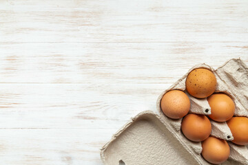 Brown eggs in open carton box on wooden background. Fresh organic chicken eggs in carton pack. Top view with copy space. Natural healthy food and organic farming concept.