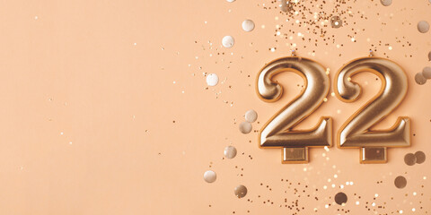 22 years celebration. Greeting banner. Gold candles in the form of number twenty two on peach background with confetti.