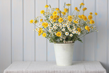 summer still life, a bouquet of white and yellow daisies in a white bucket, flowers on a table with a tablecloth on a white background.