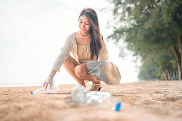 Young tourist asian woman picking plastic bottle into trash plastic bag for cleaning the beach,...