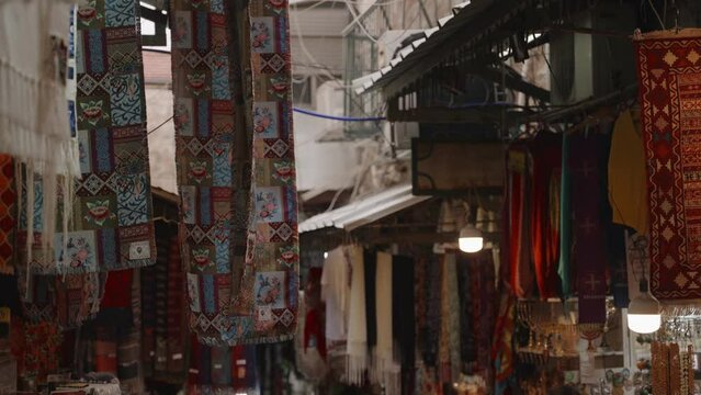 Merchandise and products in market stores in bazaar in the Old City of Jerusalem. Small narrow alley with souvenirs and religious artifacts for tourists in ancient Holy Land. Commercial fabric vendors