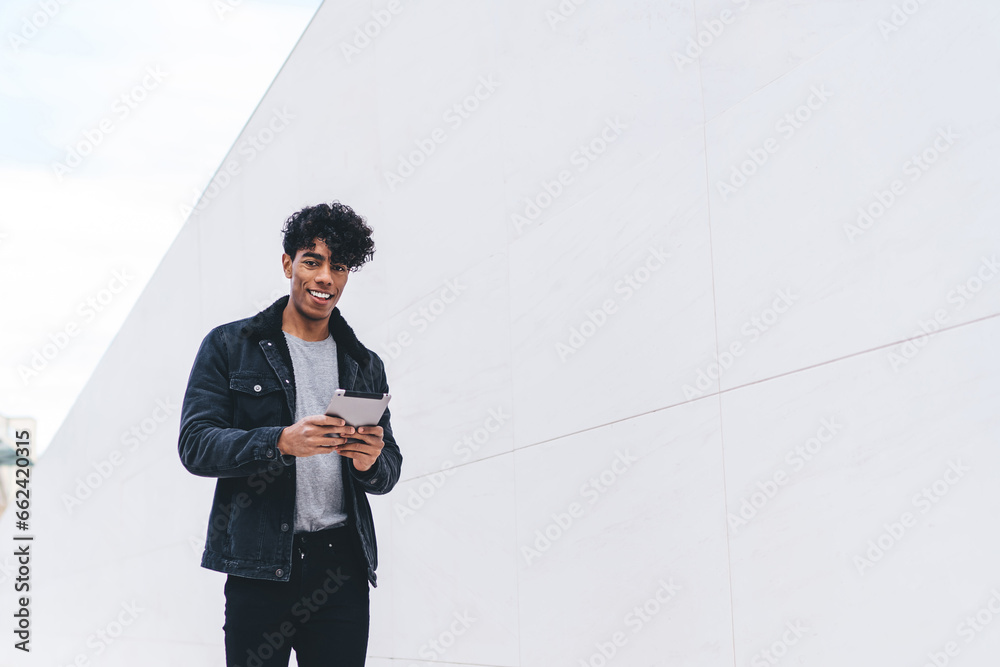 Wall mural trendy cheerful african american man using tablet while walking along urban street tunnel