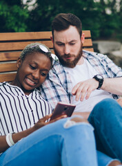 Fototapeta premium Pensive multiethnic couple using smartphones while resting in park