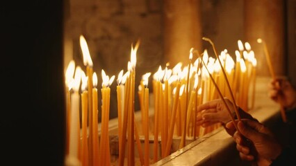 Close up - hands with candles in the Church of the Holy Sepulchre in Jerusalem. During religious visit to famous and holy site for Christianity visitors light candles for faith and prayer in church