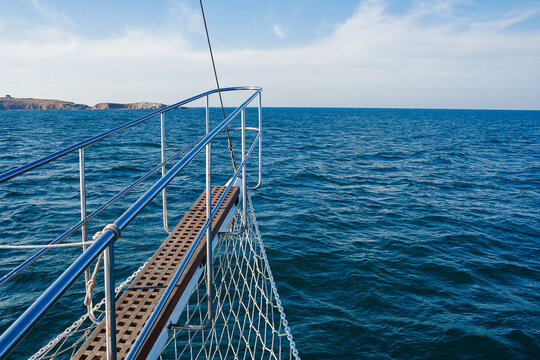 view from the nose of a ship in open sea. island in the distance on the horizon. sunny weather