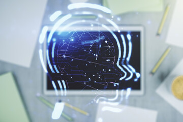 Creative artificial Intelligence concept with human head hologram and modern digital tablet on background, top view. Multiexposure