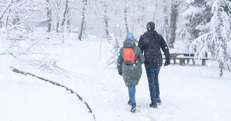 Loving couple walking in winter park in the snowfall