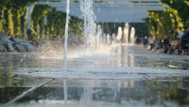 Unrecognizable little girl in rubber boots runs along the city fountain, close-up