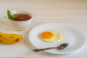 Sunny side up egg, cup of mint tea, banana on white background. Food for breakfast.