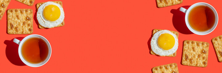 Cup of tea, crackers, sunny side egg on red background. Food for snack. Top view.