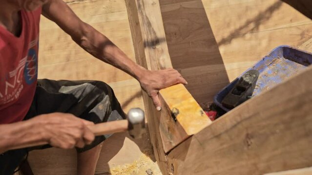 A shipbuilder hammering the triangular section of a traditional wooden fishing boat frame on the coast of Indonesia. Close up shot without showing the face.