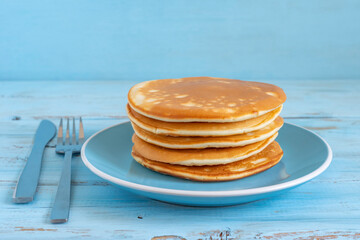 Pancakes in ceramic plate for tasty breakfast over blue wooden background.