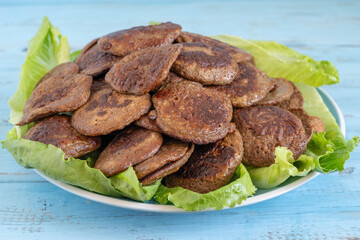 Beef liver patties on ceramic plate with lettuce leaves over blue wooden background.