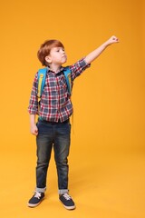 Cute schoolboy with backpack on orange background