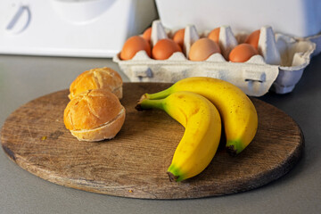 branch of bananas lies on the table with eggs and burger buns.