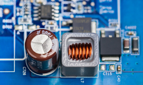 Close-up of electronic components on printed circuit board of power supply. Brown electrolytic capacitor, inductor in gray housing and black transistors or micro chip on a blue PCB. Electrotechnology.