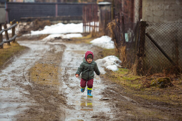 Little boy in protective rubber boots and rain clothes jumping in mud puddle. Happy child having fun while playing in puddle after rain.