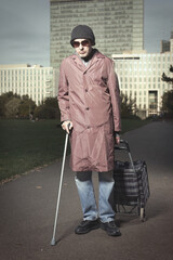 Senior citizen walking with wheel cart and stick in city park