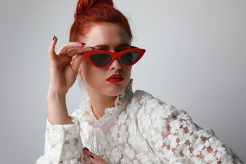 Portrait of surprised young woman wearing cat-eye sunglasses posing indoor.