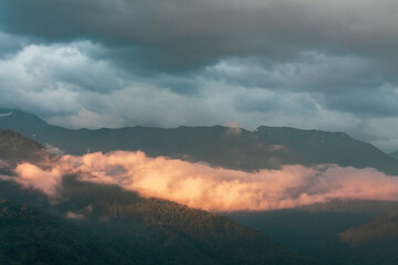 Fog and clouds in the mountains against the backdrop of the setting sun, changeable weather in the mountains, clouds and nebula on mountain peaks