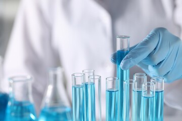 Scientist taking test tube with light blue liquid in laboratory, closeup. Space for text