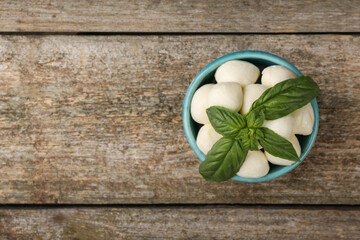 Tasty mozzarella balls and basil leaves in bowl on wooden table, top view. Space for text