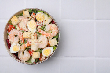 Delicious Caesar salad with shrimps on white tiled table, top view. Space for text