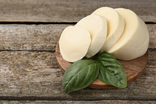 Board with tasty mozzarella slices and basil leaves on wooden table, closeup. Space for text