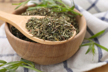 Bowl of dry tarragon and spoon on wooden table, closeup