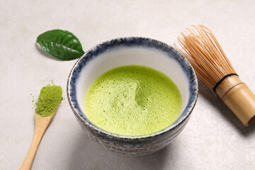 Cup of matcha tea, bamboo tools and green powder on light gray table, closeup