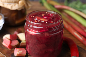 Tasty rhubarb sauce in glass jar on table, closeup view