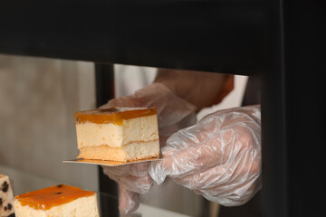 Worker taking tasty piece of cheesecake with jelly from showcase in cafe, closeup