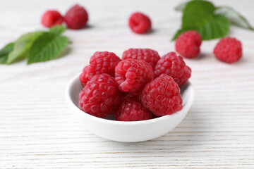 Tasty ripe raspberries in bowl on white wooden table