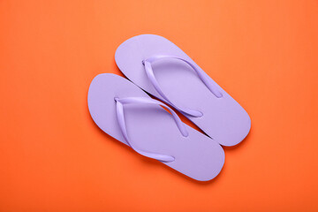 Stylish violet flip flops on orange background, top view