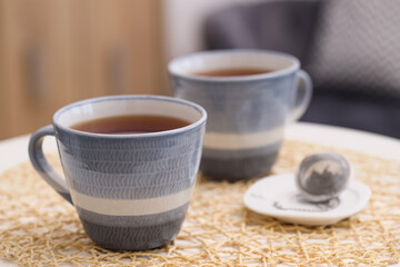 Cups of tea and snap infuser with dry leaves on table indoors, closeup. Space for text