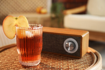 Relax at home. Glass of tasty cider and portable speaker on wicker table in room, closeup. Space for text