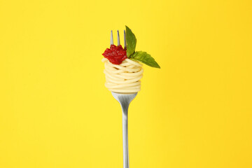 Fork with tasty pasta, tomato sauce and basil leaves on yellow background