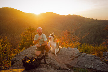 The man and best friend dog husky enjoy the time in a sunset on the mountain. 