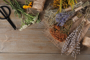 Different herbs, thread and scissors on wooden table, flat lay. Space for text