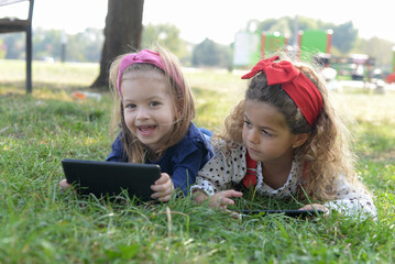 Two little girls are holding a tablet on the playground.using modern gadgets to watch videos and play games