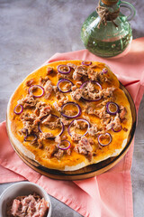 Canned tuna and onions in baked pizza on a wooden board on the table vertical view