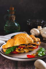 Appetizing croissant stuffed with fried champignons and tomatoes on a plate vertical view