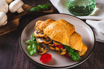 Fresh croissant with fried mushrooms, tomatoes and basil on a plate