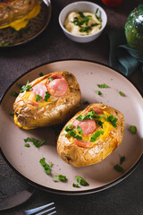 Baked potatoes in skins with egg and pieces of sausage on a plate on the table vertical view