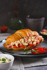 Croissant sandwich with scrambled eggs, sausages, tomatoes and herbs on a plate vertical view