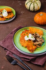 Pumpkin fritters with mushrooms and cream cheese on a green plate on a brown concrete background. Pumpkin recipes.