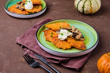 Pumpkin fritters with mushrooms and cream cheese on a green plate on a brown concrete background. Pumpkin recipes.